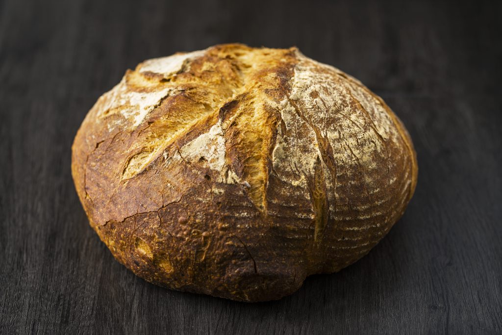 Hogaza de pan de pagès de masa madre de PANARRA, con corteza dorada y greñado curvo, sobre madera oscura