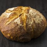 Hogaza de pan de pagès de masa madre de PANARRA, con corteza dorada y greñado curvo, sobre madera oscura