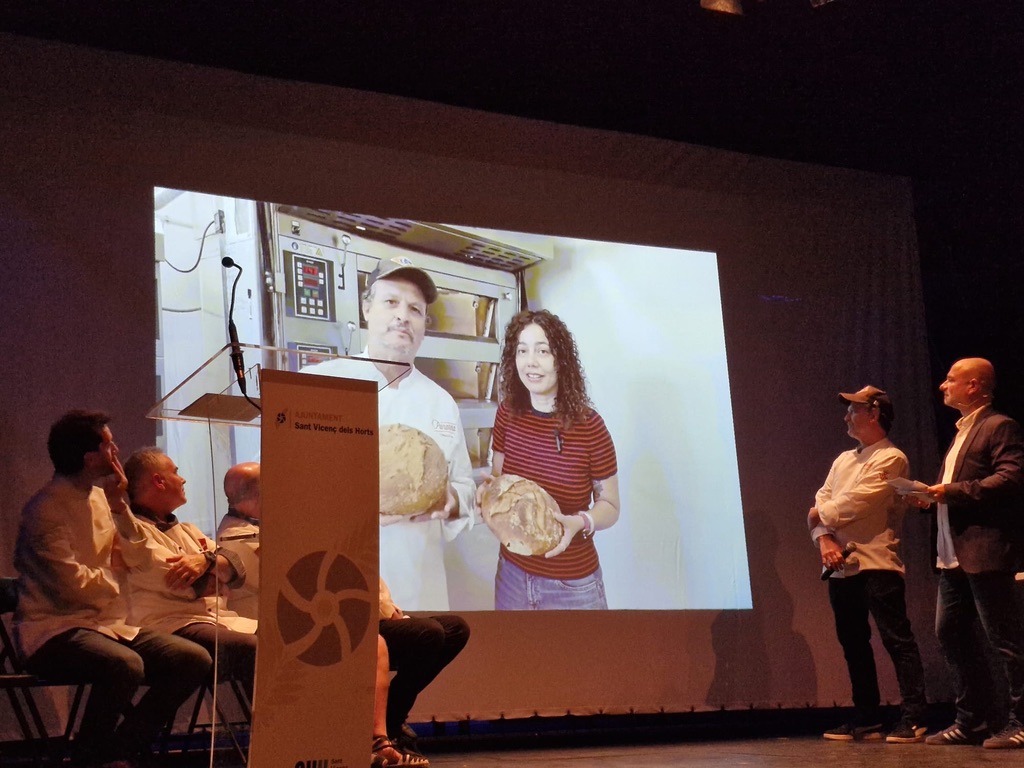 Panadero y colaboradora de Panarra mostrando el pan de pagès en la pantalla de la final del concurso